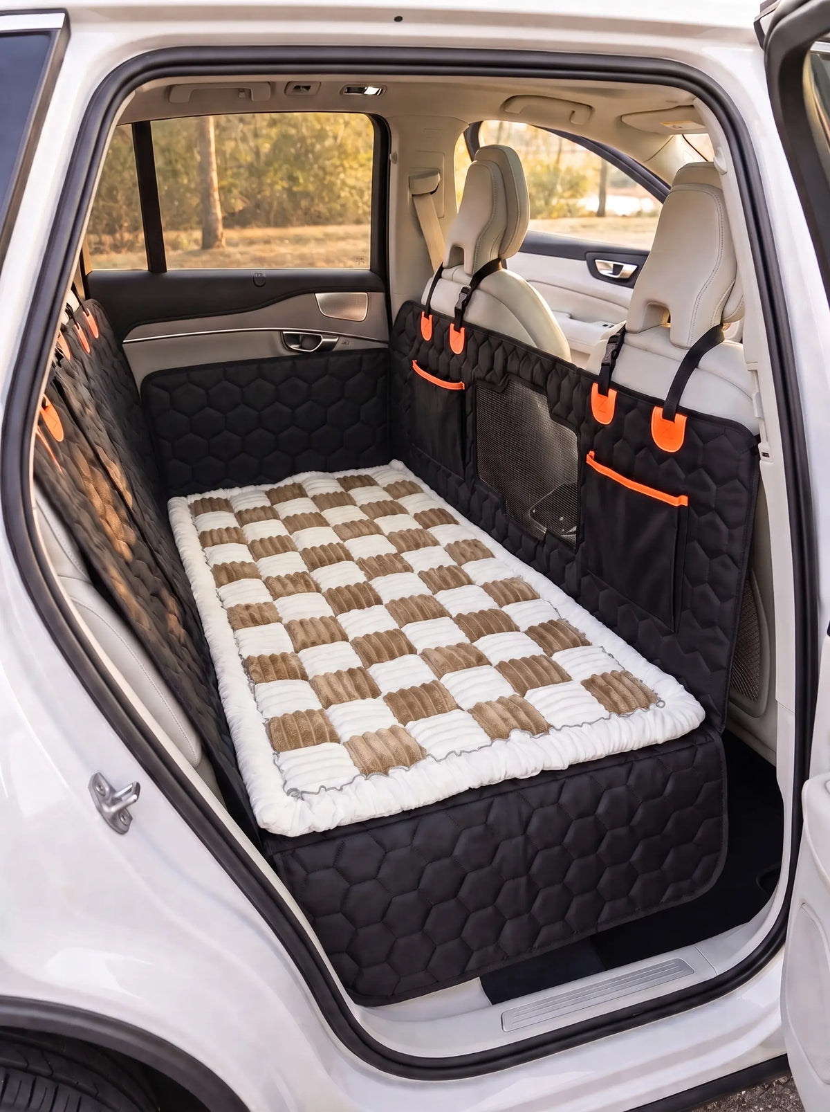 A pet car bed with a brown and white checkered pattern and a white faux fur trim, shown installed in the back of a white SUV. The bed is fitted between the rear seats on top of the silverhammock car seat cover