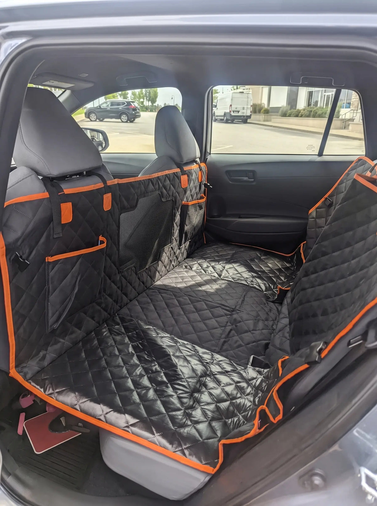 A black quilted pet Silverhammock car seat cover set with bright orange trim and side pockets, shown installed across the rear seats of a vehicle.